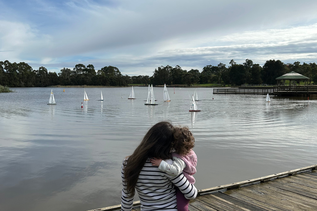 A mother holds her young child and looks out at boats on the water.